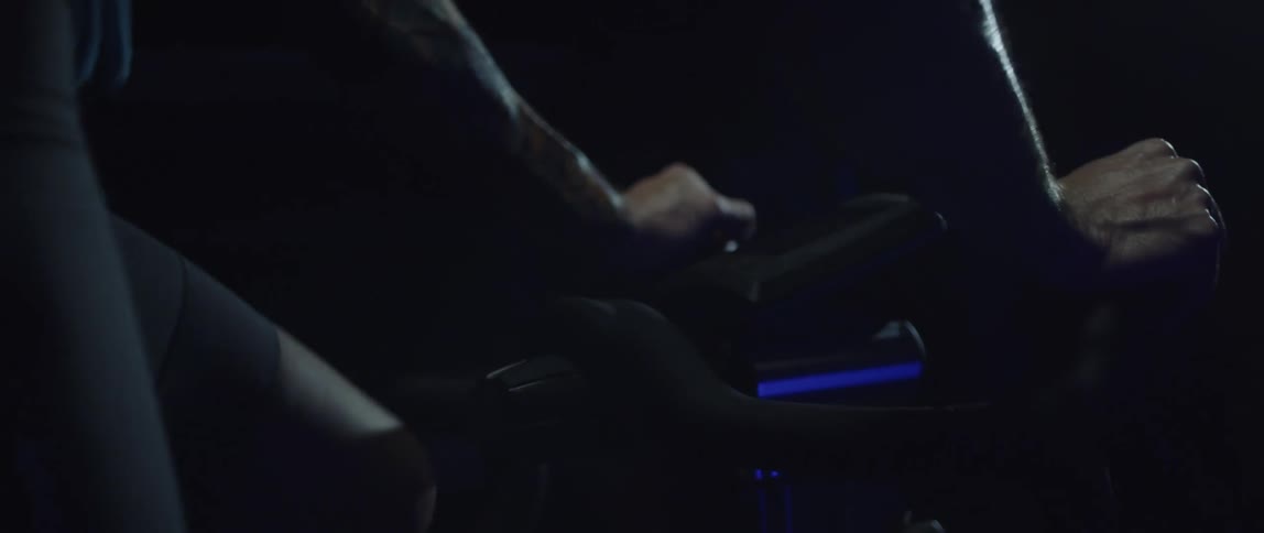 Athletic man gripping the handlebar and exercising on a stationary bike in a dark room