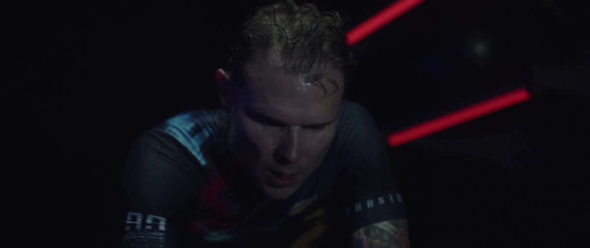 Exhausted athletic man wearing cycling jersey riding a stationary bike and sweating a lot