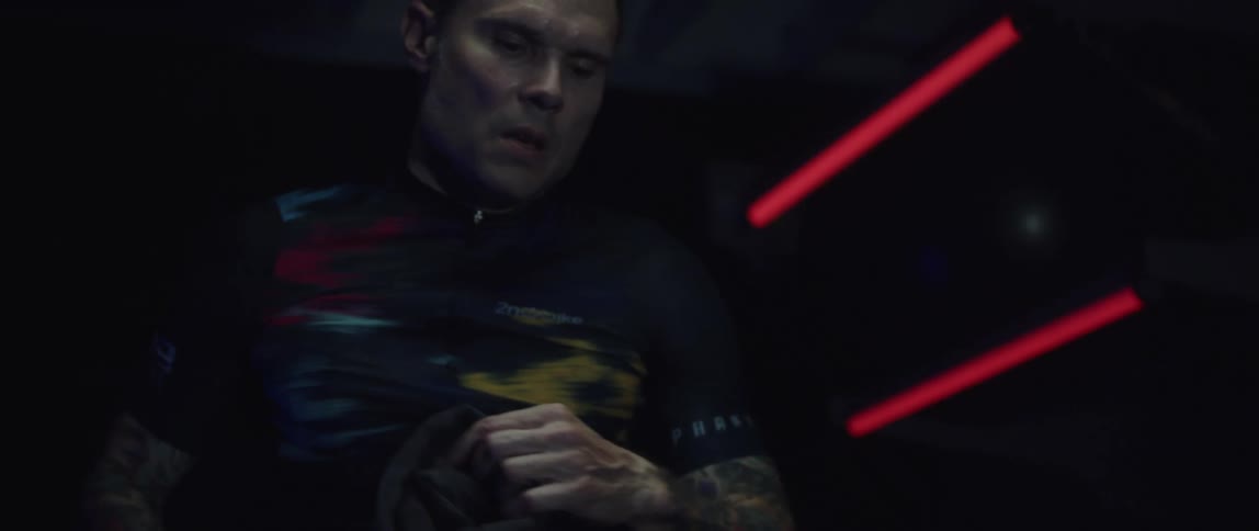 Focused cyclist man exercising on a stationary bike on a dark room and drying off his sweat with a face towel