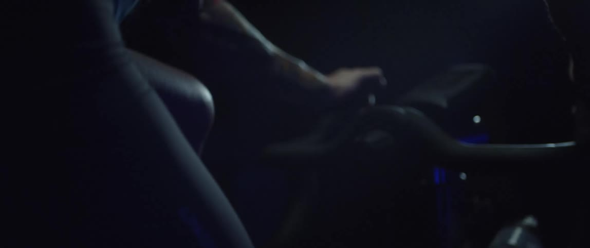 Close up of the hands of a man gripping the handlebar of a bicycle while pedaling under blue lights