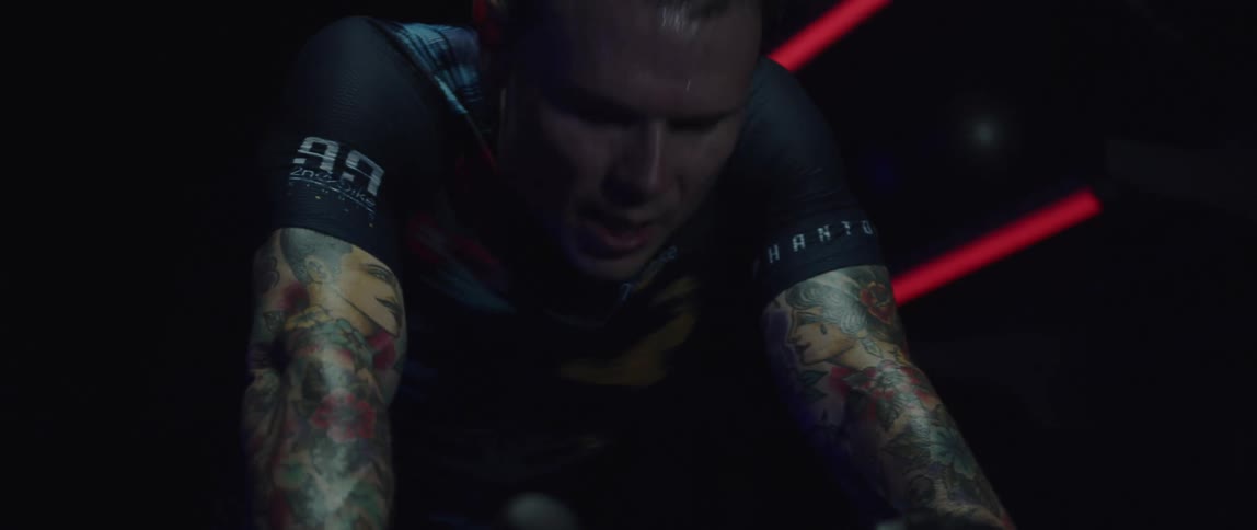 Exhausted man with tattooed arms wearing cycling jersey riding a stationary bike
