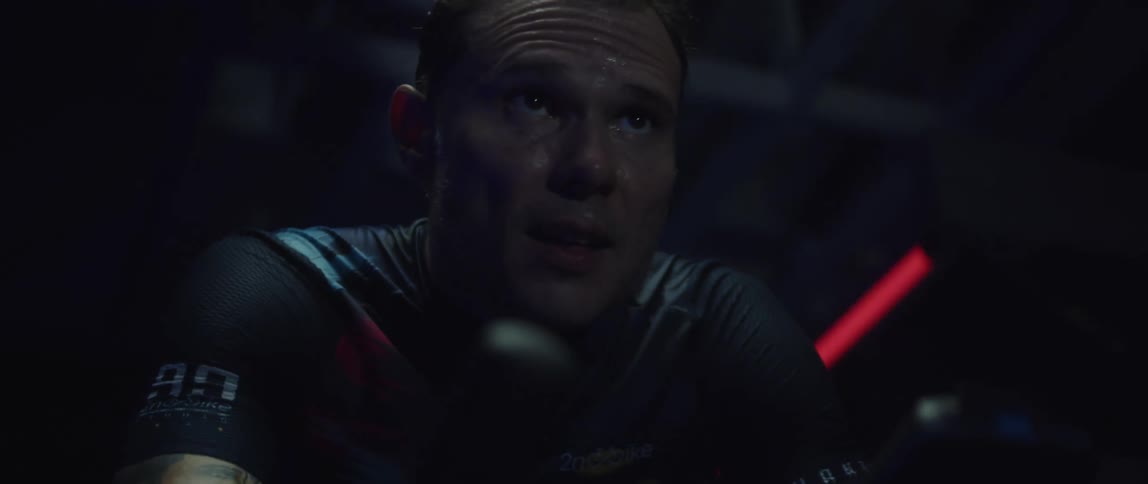 A man sweating man pedals an exercise bike in a dark room