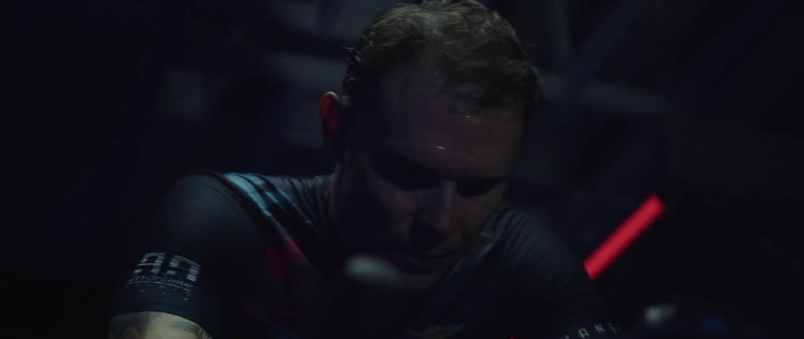 Determined and sweaty male cyclist with jersey shirt and tattoos rides exercise bike