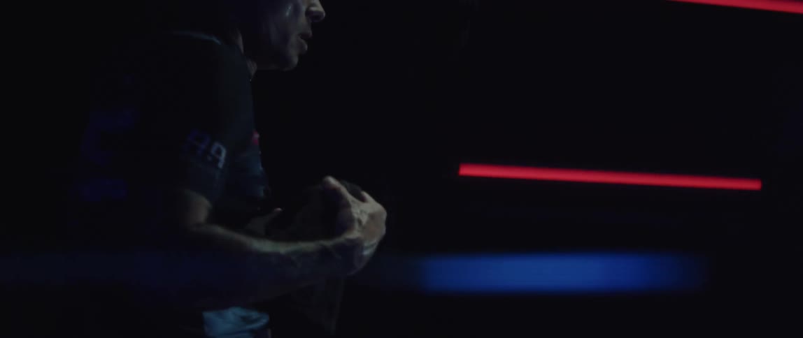 A sweaty man exercising on a stationary bike in a dimly lit room
