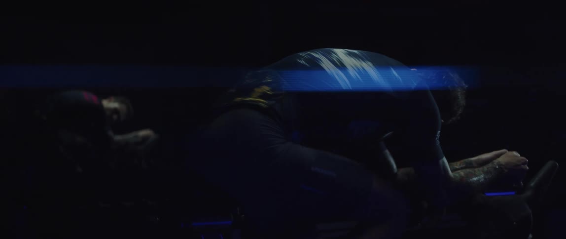 Cyclist wearing a cycling jersey exercising on a stationary bike and looking at himself in the mirror at his side in a dark room