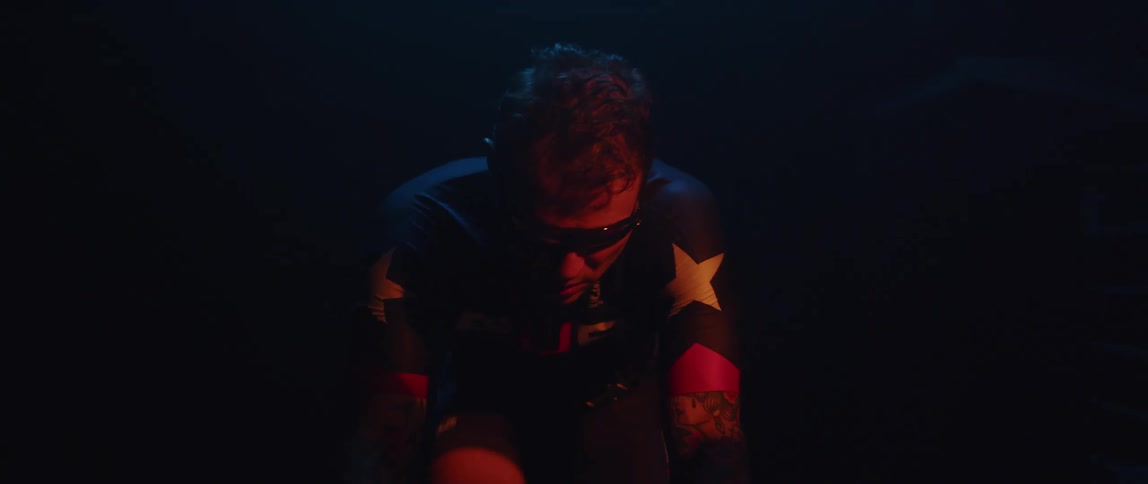 Man pedaling on a static bicycle inside a dimly lit room against a dark background