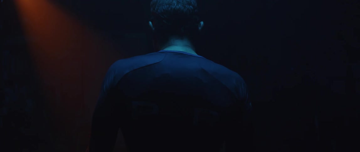 Man breathes deeply shrugging his shoulders and tipping his head back in dark room lit by red lighting