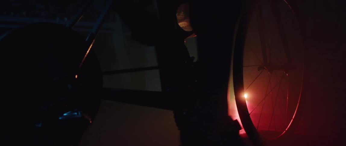 A person pedals an exercise bike in a dark room dimly illuminated by a red light