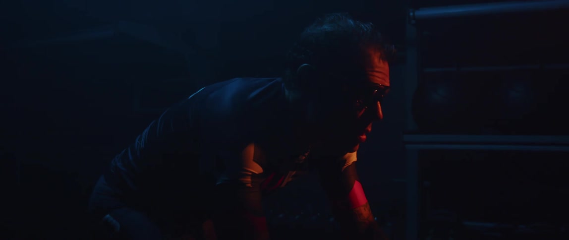 A man with sunglasses on is riding a bike in the dark