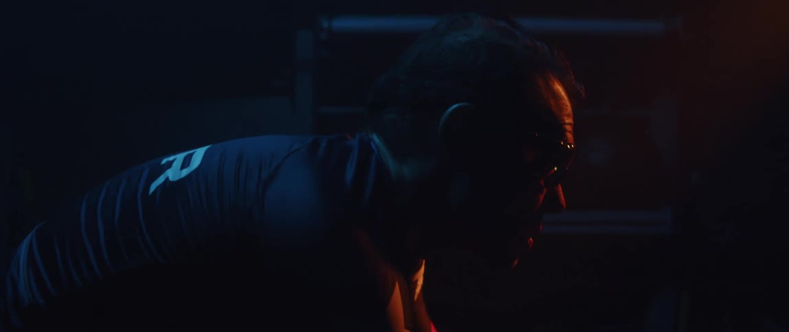 Focused man wearing a cycling jersey and cycling glasses riding a stationary bike in a dark gym room