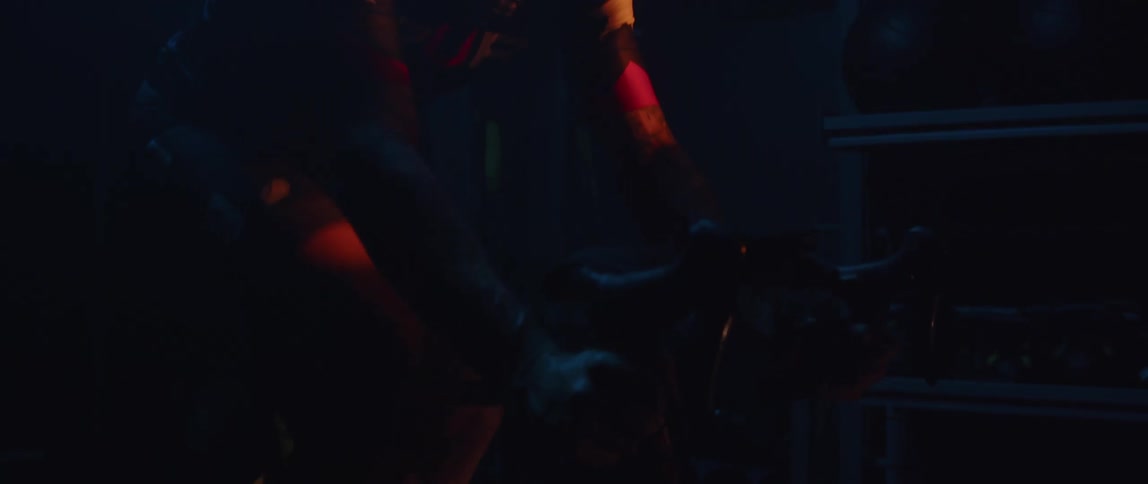 Man wearing sunglasses pedaling a static bicycle inside a dimly lit room