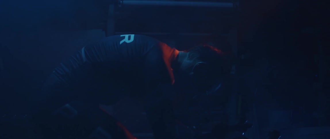 Focused athletic man wearing a cycling jersey riding a stationary bike in a dark gym room