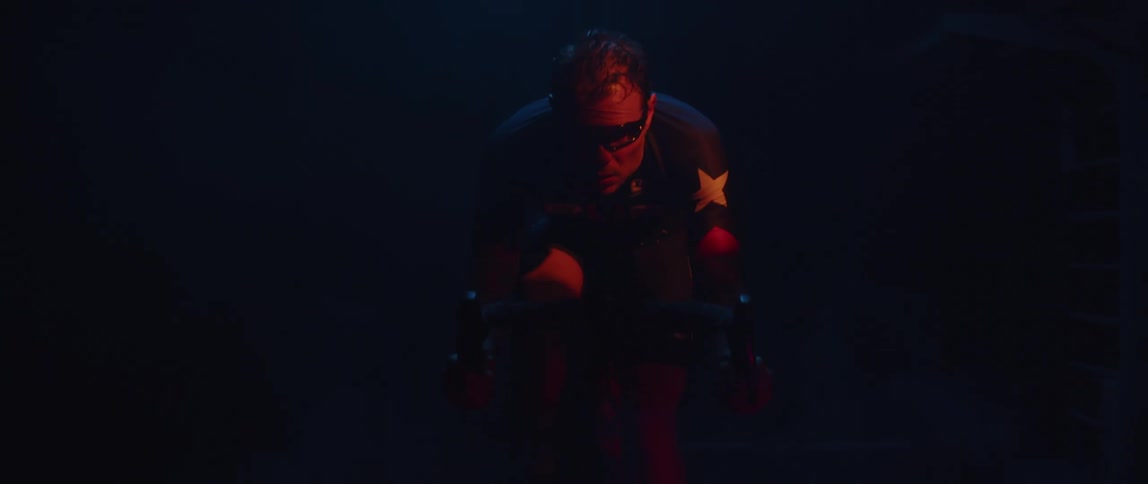Determined male cyclist with jersey shirt and tattoos rides exercise bike in red light
