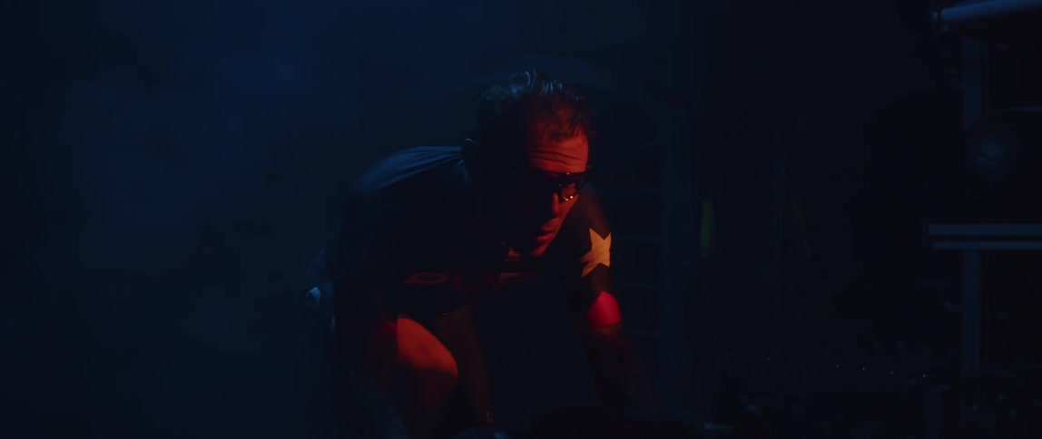 Focused man wearing a cycling jersey and cycling glasses exercising on a stationary bike in a dark gym room