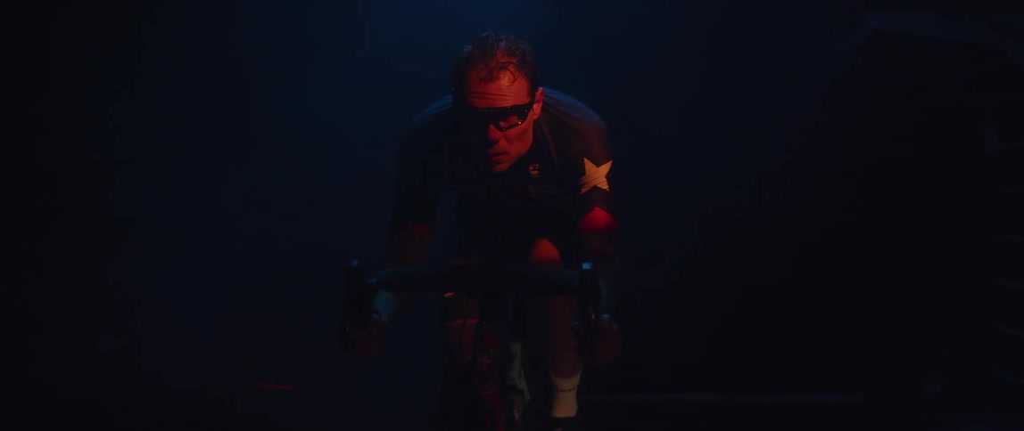 A man looks exhausted as he pedals on exercise equipment in a poorly lit room