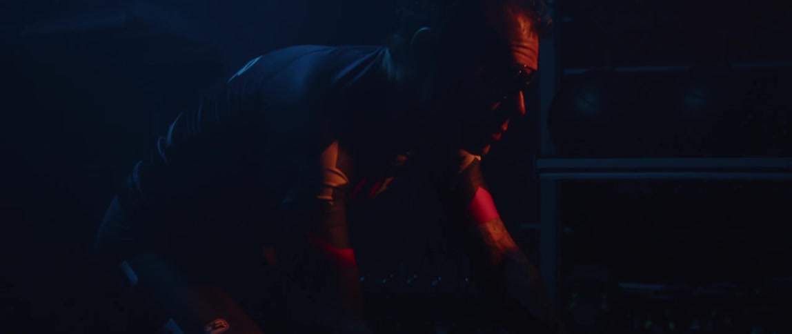 Cyclist wearing a cycling jersey and cycling glasses exercising on a stationary bike in a dark gym room