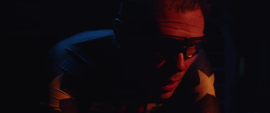 Male cyclist wearing cycling glasses and a cycling jersey training on a stationary bike in a dark room