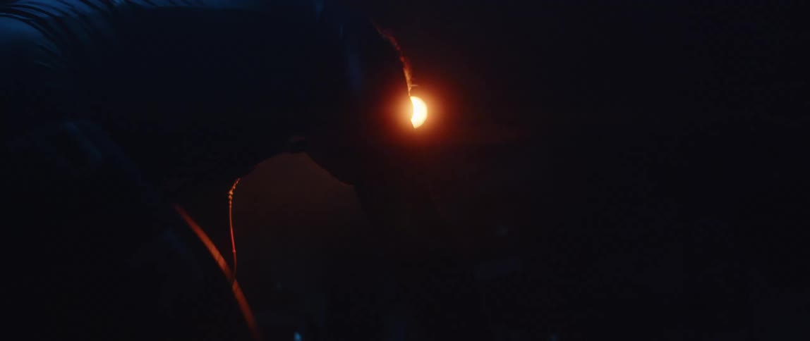 Man riding a stationary bike in a dark room with only a orange led light above him