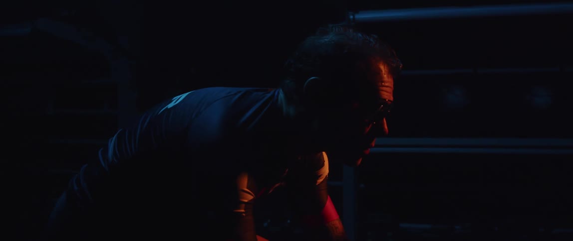 Cyclist wearing a cycling jersey and cycling glasses exercising on a stationary bike in a dark gym room