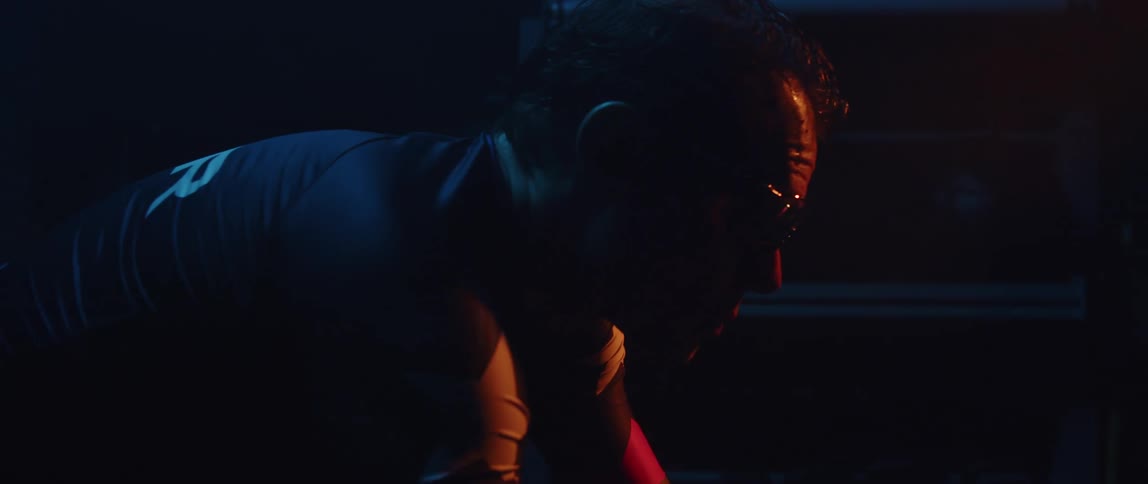 Man pedaling on a static bicycle inside a dimly lit room against a dark background