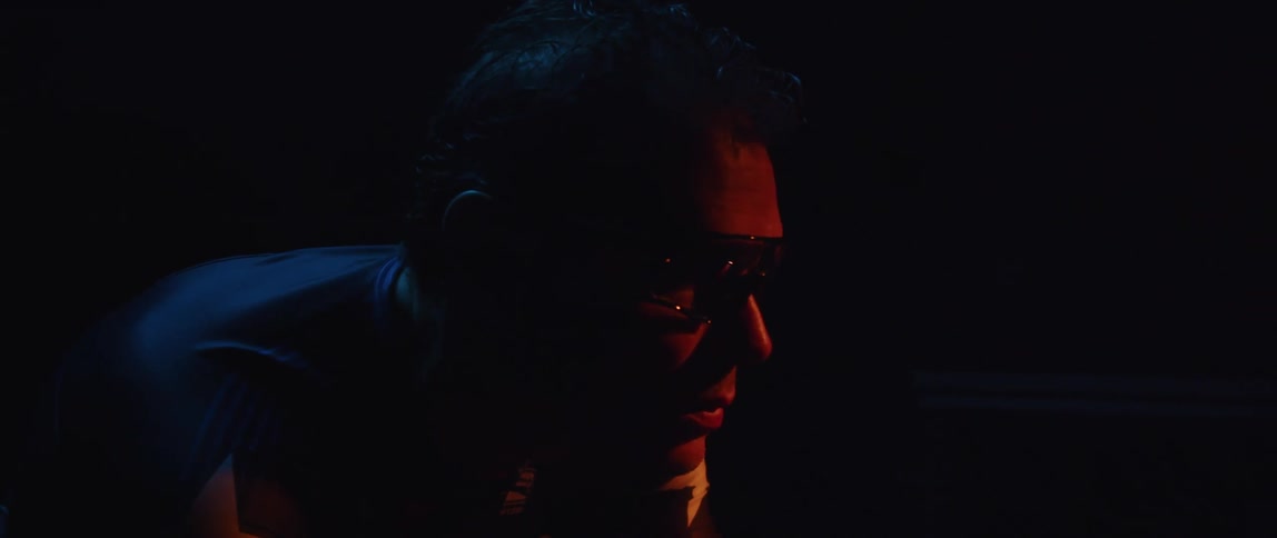 Man pedaling on a static bicycle inside a dimly lit room against a dark background