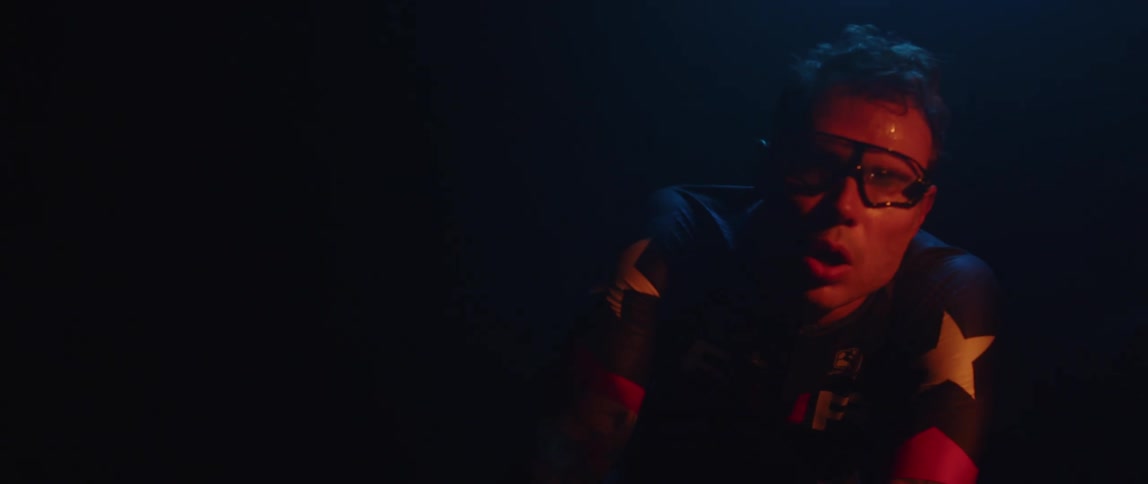 Focused sweaty man wearing cycling glasses heavy breathing while sitting on a stationary bike in a dark room