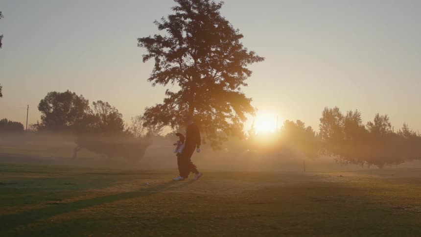 A man walks on a golf course and sets his bag down