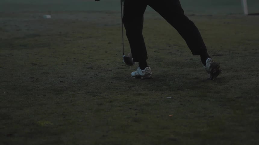 A golfer bends to put a ball and tee into the grass on a gray foggy day