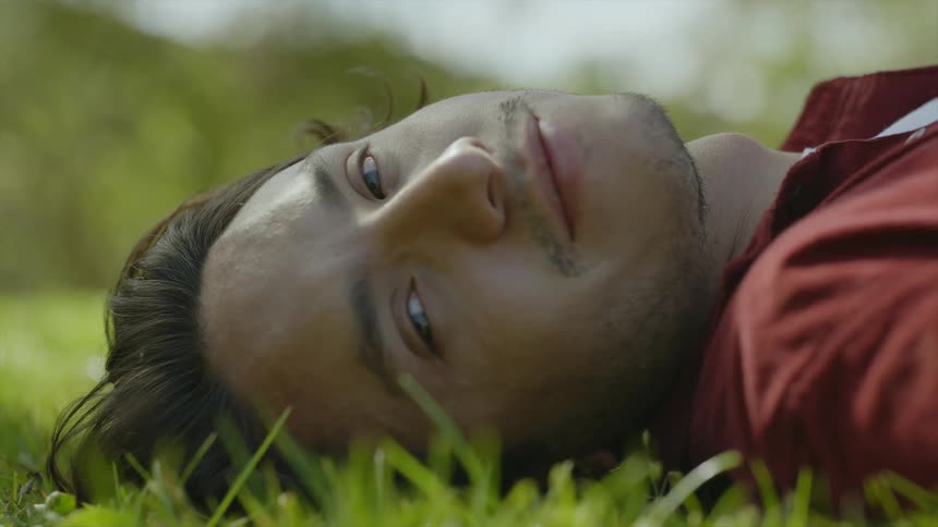 A man turns his head and smiles while lying in grass