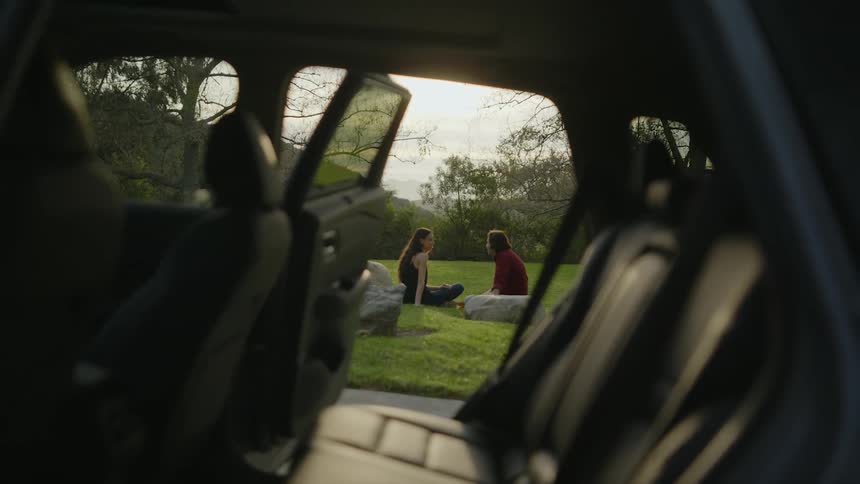 Man and woman are visible through two open car doors as they sit on grass
