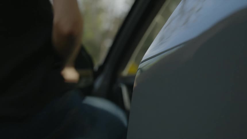 A person opens the drivers side of an automobile and gets inside and closes the door
