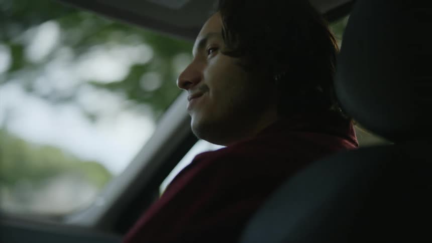 Young man sitting on the passenger seat of a car driving on a neighborhood at morning