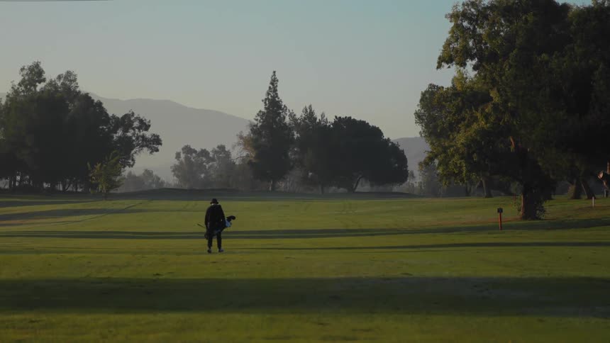 A golfer carrying their bag and a club as they walk across an empty course
