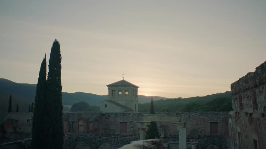 A stone building sits behind ruins