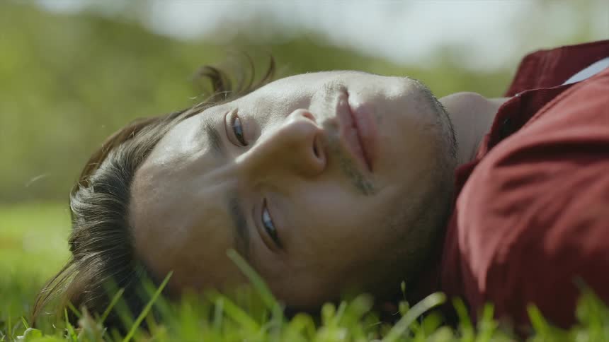 A man resting in the grass turns his head then goes back to napping