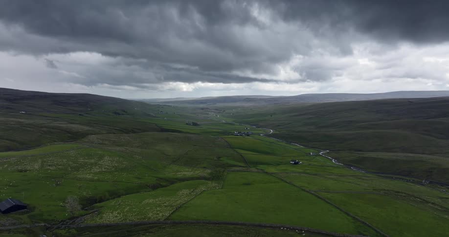 A curving stream with farmhouses and lush green fields under a gray cloudy sky