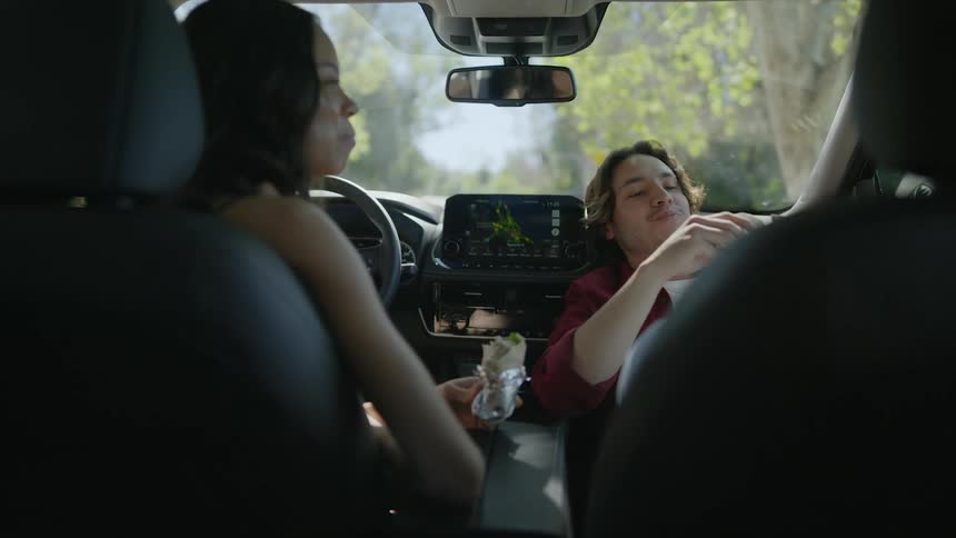 A man and woman eat burritos in their parked car