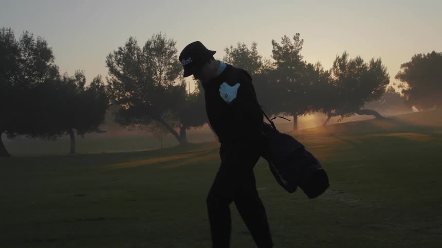 A male golfer walks along the golf course while carrying his golf club bag