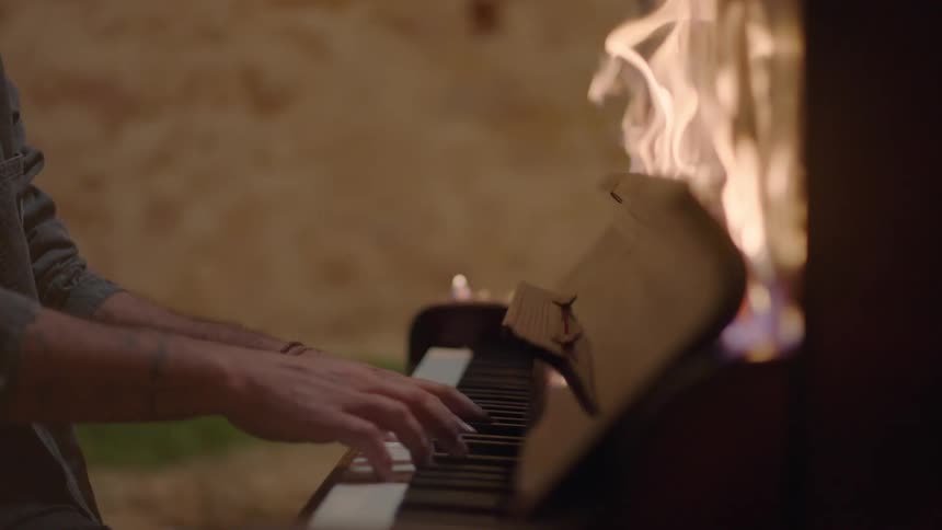 A man plays an upright piano with flames burning above the keys