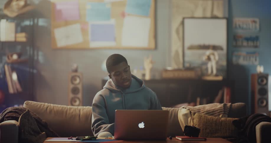 A man goes through his digital camera while sitting on the couch in front of a laptop