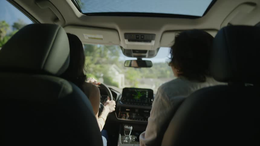 A man and woman laugh and talks as the woman drives down a neighborhood street