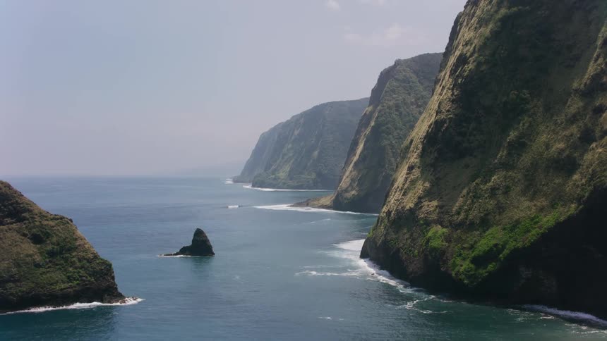 Large rocks are in the water and waves roll into shore along the coastal escarpment