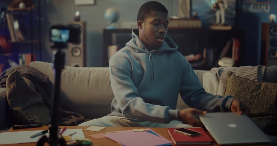 Man sits in living room making video recording as he talks about laptop
