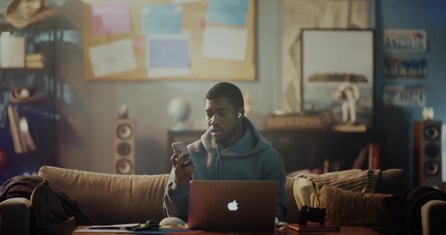A man typing on his laptop checks his phone then closes the laptop and carries it away
