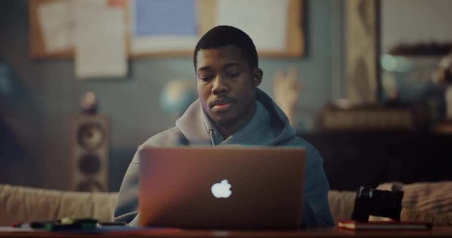 A man is sitting at a table typing on a laptop computer and he closes the lid and takes it with him as he walks away