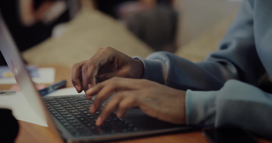 A man is sitting at a table typing on a laptop computer and he closes the lid and picks up the laptop