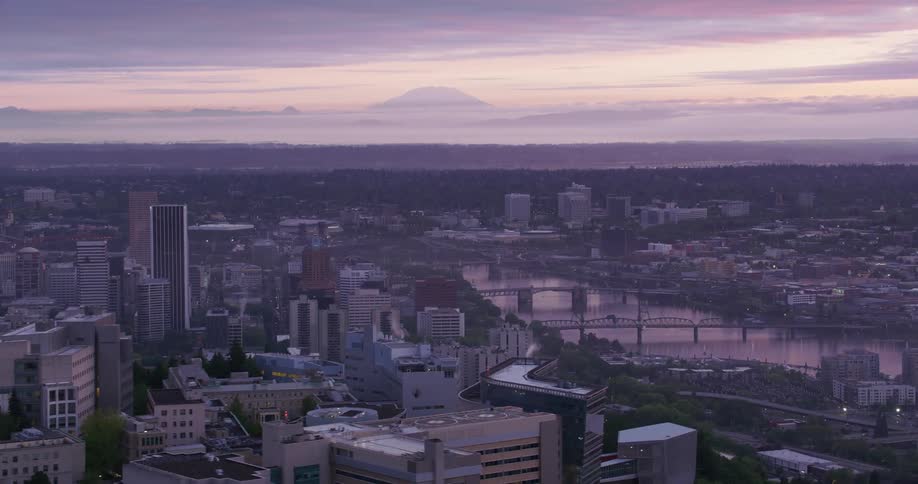 Several bridges over a river with city skyscrapers and buildings and mountain silhouette on the horizon