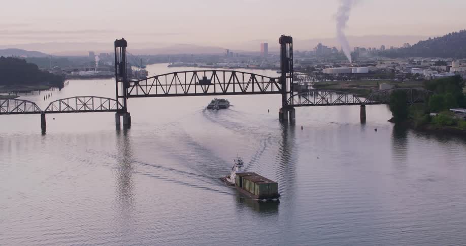 An aerial view of a shipping boat on a river with a refinery in the background