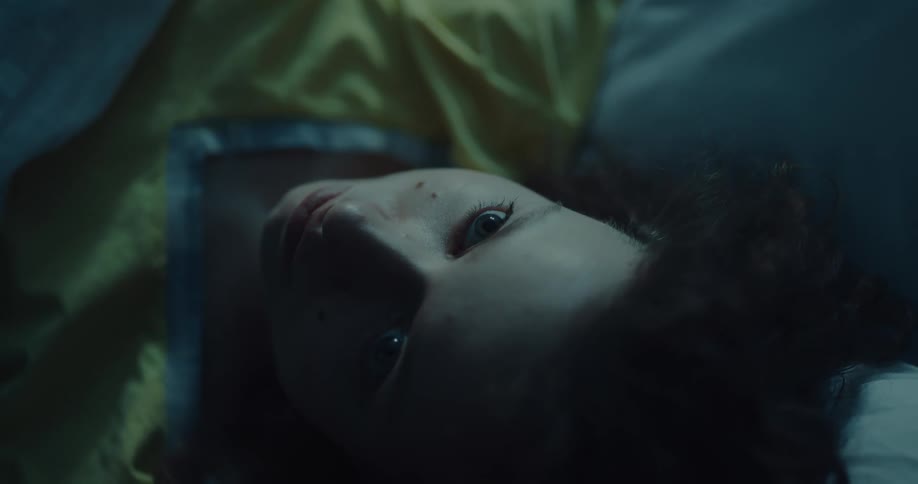A young woman stares up at the ceiling for a moment before closing her eyes while resting in bed