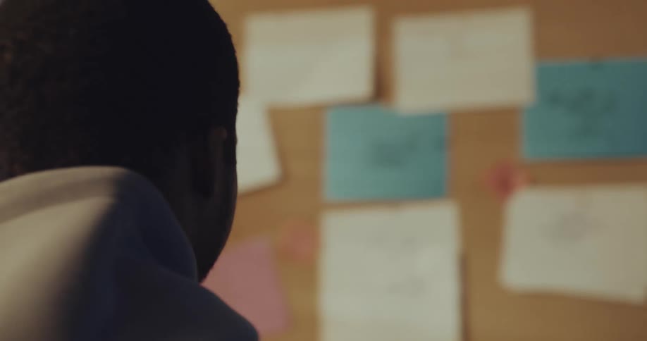 A man walks to a bulletin board to look at the papers hanging on it